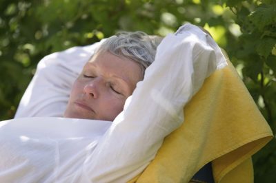 Senior woman with white hairs sleeping on lounger in her garden.
